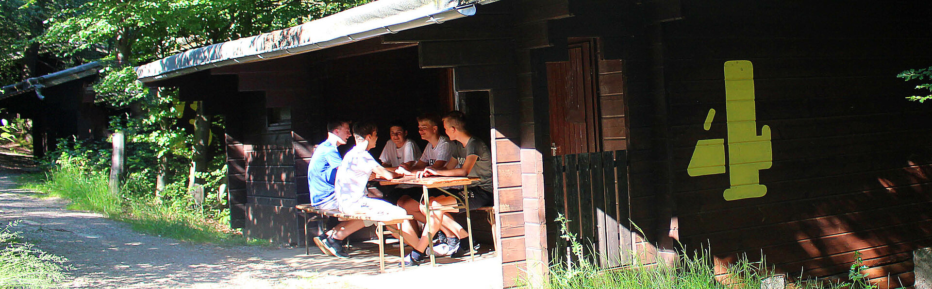 Die Jungs von der Ferienfreizeit unterhalten sich angeregt vor dem Blockhaus im Abenteuercamp.