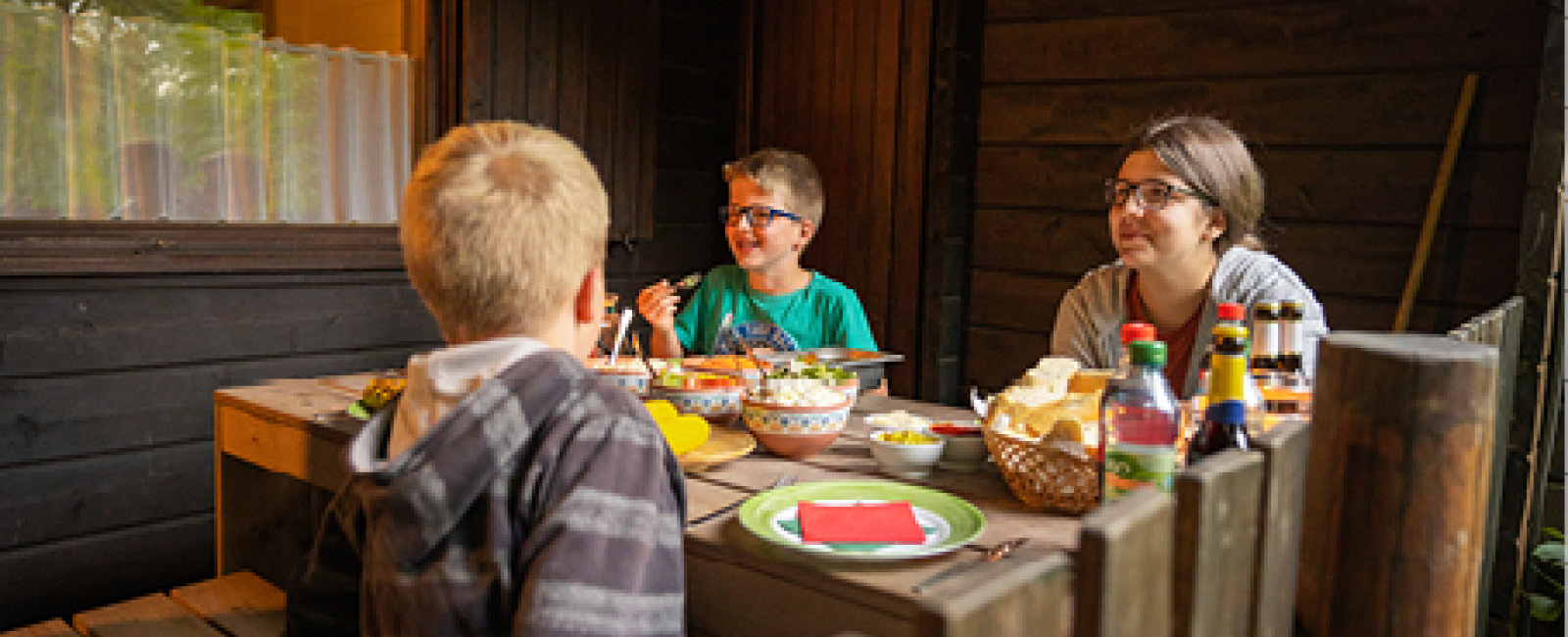 Die beiden Jungs haben Spaß beim Abendessen mit ihrer Mutter auf der Terrasse vor dem Blockhaus.