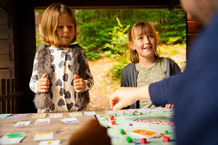 Zwei Mädchen spielen im Blockhaus mit ihrem Papa Monopoly.