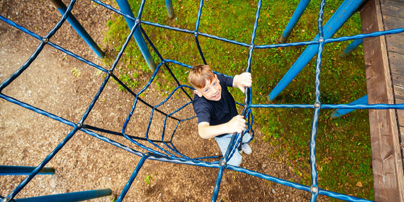 Der Junge klettert auf dem Kinderspielplatz und hat viel Spaß dabei.