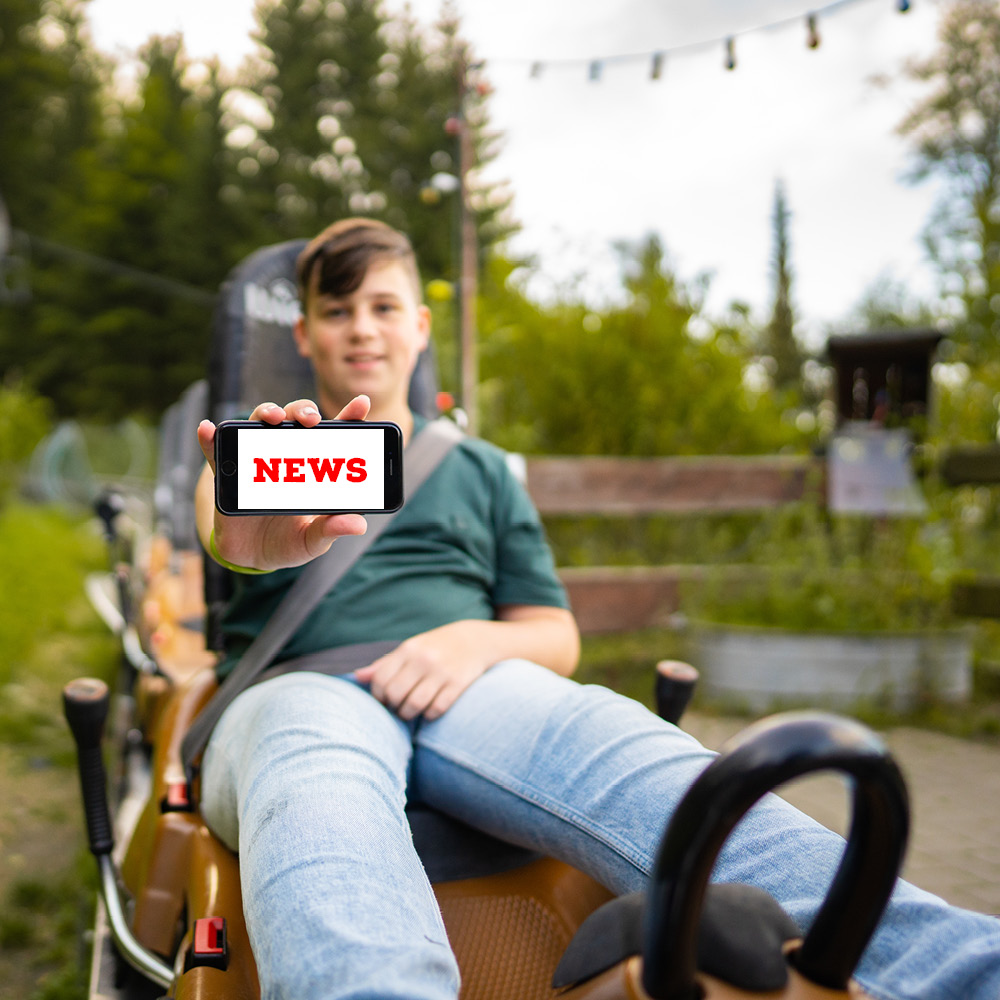 Der Junge im Trapper Slider zeigt auf seinem Handy den FORT FUN Newsletter.