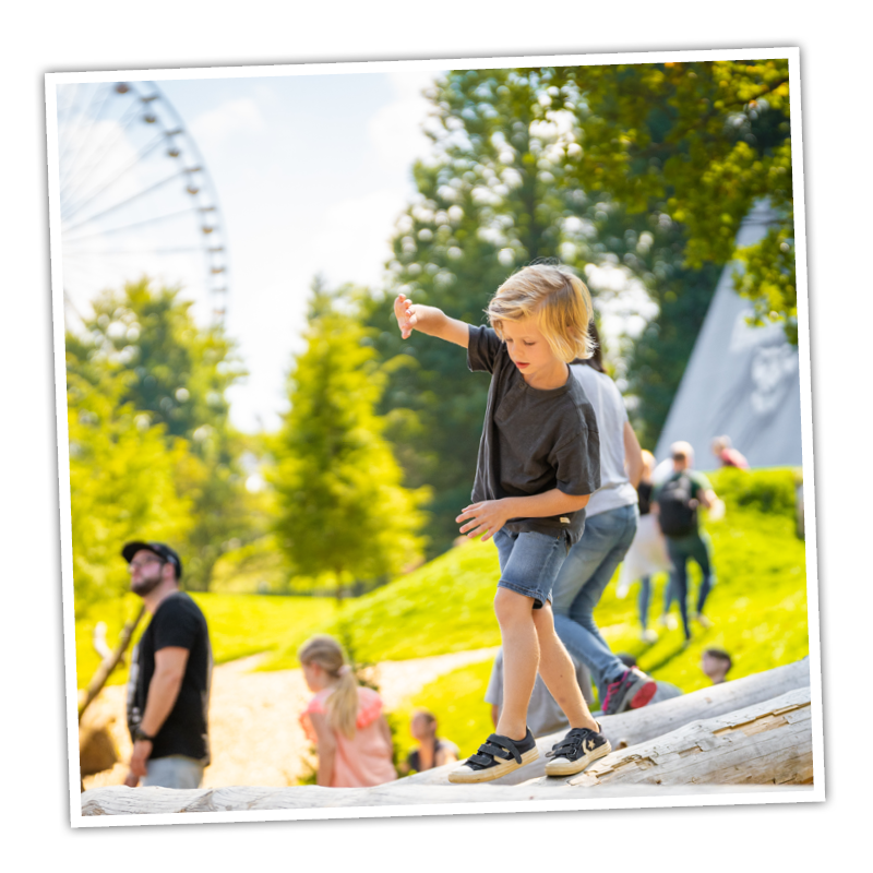 Der Junge balanciert auf einem Baumstamm in der Adventure Area und macht seine Naturerfahrungen.